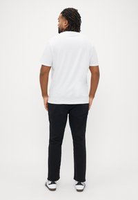 Λευκή κοντομάνικη μπλούζα με άνετη εφαρμογή, συνδυασμένη με στενά μαύρα παντελόνια και λευκά αθλητικά παπούτσια με μαύρες λεπτομέρειες. Χωρίς ορατά σχέδια.