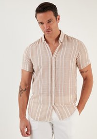 Camisa de manga corta, abotonada, en color beige con rayas verticales blancas. Hecha de un tejido texturizado con un corte relajado y un dobladillo curvado.
