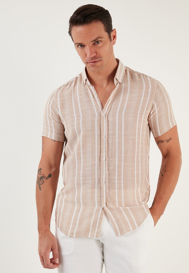 Camisa de manga corta, abotonada, en color beige con rayas verticales blancas. Hecha de un tejido texturizado con un corte relajado y un dobladillo curvado.