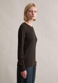 Brązowa, prążkowana bluzka z długim rękawem i okrągłym dekoltem, z dopasowanymi mankietami i wąskim krojem. Noszona z luźnymi niebieskimi spodniami.