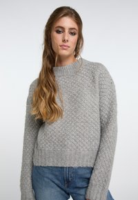 Pulover gri din tricot cu un model texturat, decolteu rotund și manșete cu dantelă. Asociat cu blugi denim albaștri. Material moale și cald.