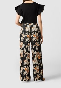 Haut noir avec des manches volantes associé à un pantalon à larges jambes à motifs floraux, featuring des motifs orange et crème sur fond noir.