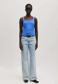 Blauwe tanktop met vierkante halslijn, gecombineerd met lichtblauwe wijde jeans, afgewerkt met een zwarte riem en zonnebril. Glad katoenen textuur.