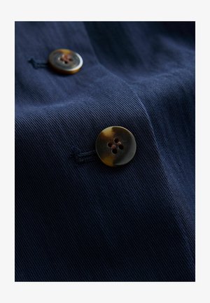 Navy tyg närbild med två knappar, en stor med ett sköldpaddsmönster och fyra hål, sydd med kontrasterande mörktråd.