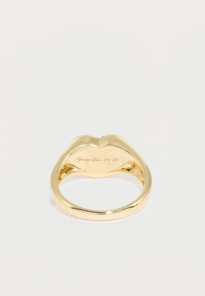 Zlatý prsteň s textúrovaným, sochárskym dizajnom pripomínajúcim pery. Na vnútornej strane obrúčky je vyrytý nápis "Yvonne Léon 375". Vysokolesklý povrch.