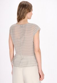 Leichtes, semi-transparentes Oberteil mit einem geometrischen Kettenmuster in Beige und Grau. Kurzärmel und Peplumsaumdetail an der Taille.