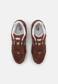 Ett par bruna och vita New Balance löparskor med mesh och mocka, sedd ovanifrån på en vit bakgrund.