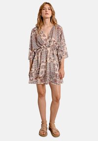 Abito floreale corto in beige chiaro con cintura da annodare, maniche lunghe e intricate trame di farfalle e fogliame. Tessuto leggero.