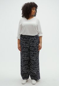 Άσπρο μακρυμάνικο τοπ συνδυασμένο με άνετο, ναυτικό μπλε παντελόνι με άσπρα αφηρημένα σχέδια, φορεμένο με λευκά αθλητικά παπούτσια.