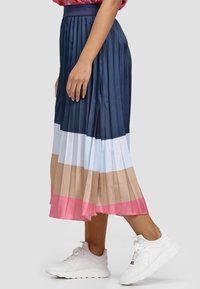 Plisseret midi-nederdel med en mørkeblå overdel, der går over i lyseblå, beige og pink. Båret med hvide sneakers.