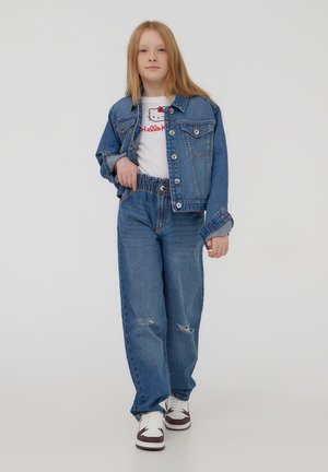 Giacca di denim, T-shirt bianca con stampa di Hello Kitty, jeans blu larghi con dettagli strappati e sneakers bianche con accenti scuri.