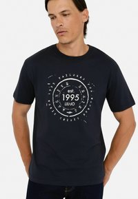 Tamno plava pamučna majica s bijelim grafičkim dizajnom sa kružnim obrascima i tekstom, okruglim izrezom i kratkim rukavima.