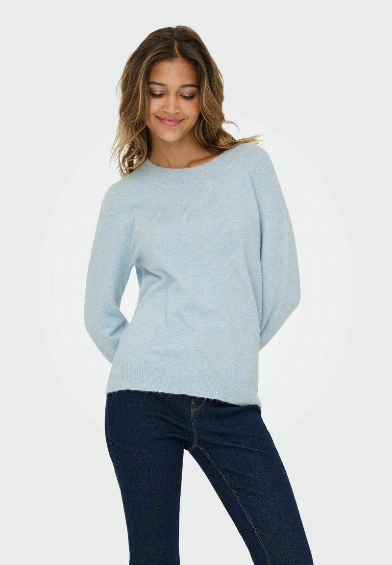 Light blue knitted sweater with a relaxed fit, round neckline, and ribbed hem, paired with dark blue jeans. Smoothing texture visible.