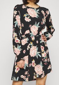 Svart blommig klänning med långa ärmar, rund halsringning, elastisk midja och stora rosa rosor med gröna blad.