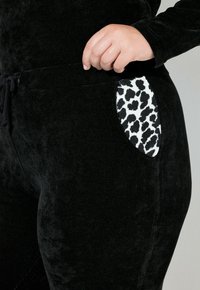 Zwarte corduroy joggers met een luipaardprint zakdetails. De stof lijkt zacht en heeft een gestructureerd patroon met verticale lijnen en een elastische tailleband.