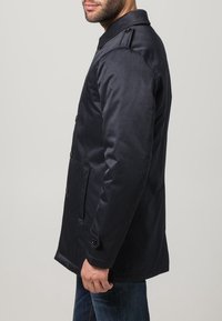 Mörkblå midjelång rock med slät textur, försedd med knappstängning, slagkrage och sidofickor. Accentuerad med subtila axelklaffar.