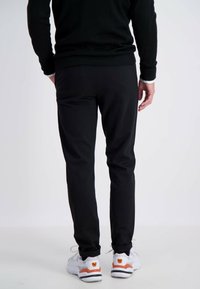 Zwarte taps toelopende broek met een gladde textuur, omgeslagen zoom, gecombineerd met witte sneakers met oranje en zwarte accenten.