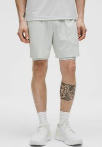 Ljust grå sportshorts med dragsko i midjan, sidofickor och en mjuk textur, ihop med vita sneakers och ankelsockor.
