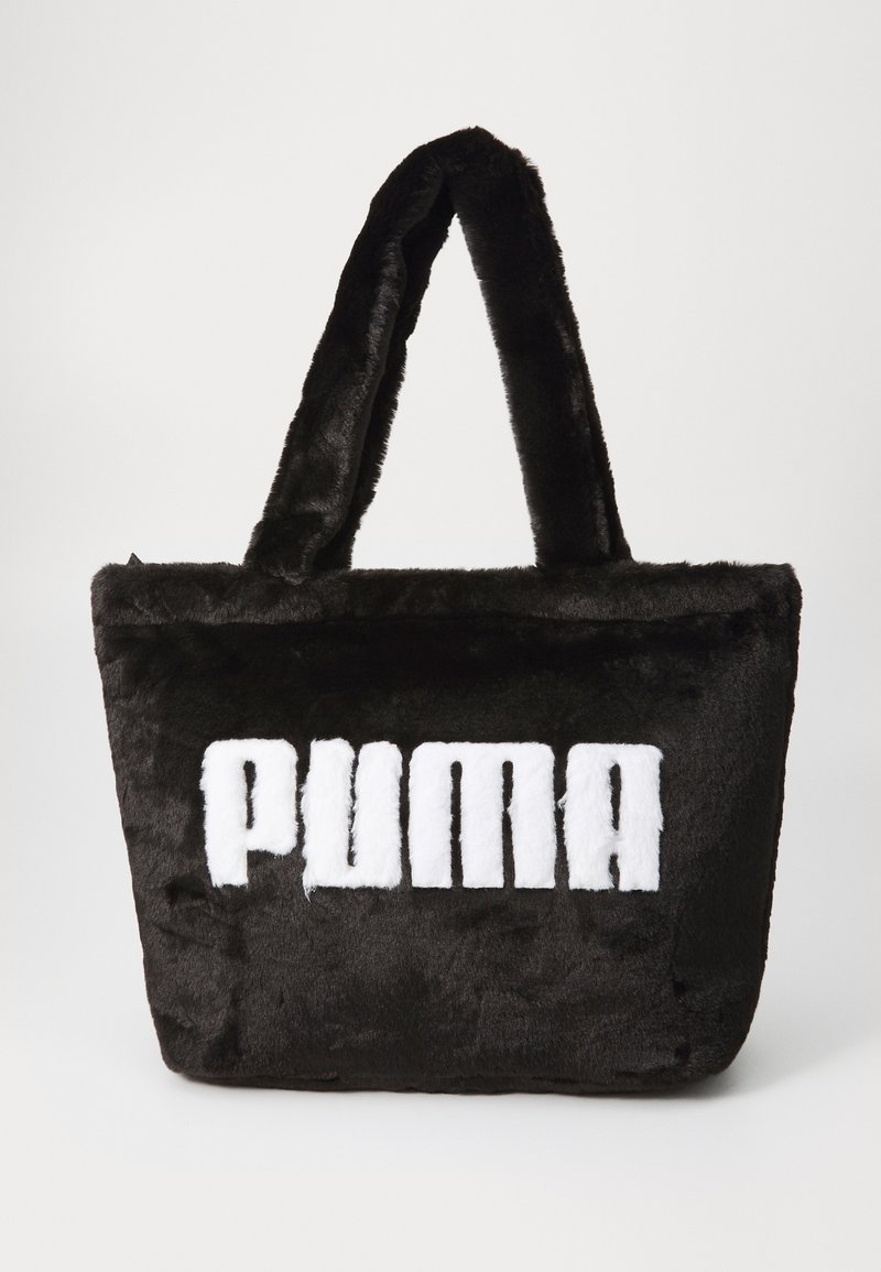 Sac fourre-tout en fausse fourrure noire avec une texture pelucheuse, ornée d'un logo "PUMA" blanc bien visible à l'avant et de doubles poignées en tissu.