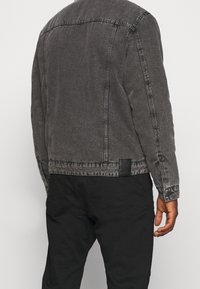 Grijze spijkerjasje met een vervaagde afwerking, voorzien van een klassieke kraag, geruite manchetten en een rechthoekig zwart lederen detail aan de achterkant.