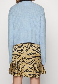 Vaaleansininen ribbineulottu neule pitkine hihoineen, yhdistettynä kultaisenväriseen hameeseen, jossa on mustat tiikeriraitakuviot ja röyhelöreuna.