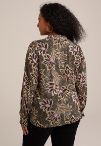 Blusa a maniche lunghe di colore verde scuro con motivo floreale. Presenta dettagli in paillettes viola e oro. Tessuto morbido con finitura testurizzata.