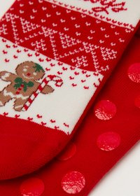 Chaussettes rouges et blanches ornées d'un bonhomme en pain d'épice avec un bâton de sucre d'orge. Le tissu rouge présente des pois brillants et des sections à motifs.
