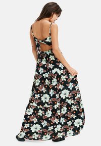 Maxikleid mit floralem Muster in Schwarz, mit figurbetontem Oberteil, Spaghettiträgern und einem offenen Rücken, der mit einer Schleife gebunden ist. Fließender, gestufter Saum.