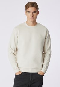 Felpa color crema chiaro realizzata in morbido cotone. Presenta polsini e orlo a costine, con un piccolo logo ricamato sul petto. Design semplice.