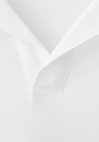 Nahaufnahme eines weißen, strukturierten Poloshirt-Kragens mit V-förmigem Ausschnitt und sichtbaren Nähten.