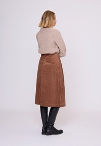 Brun kordfløjlssuggest med høj talje og sidelommer, parret med en lys beige sweater. Modellen har knæhøje sorte støvler på.