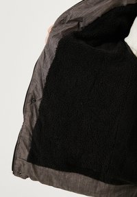 Musta fleece-vuori, jossa on teksturoidun näköinen pinta, harmaan kudotun ulkokuoren sisällä. Varustettu painonapeilla ja pehmeällä, mukavalla sisäpuolella.