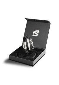 Black leather bracelet with silver accents, displayed in a black box with logo. Features braided texture and shiny metallic clasp.