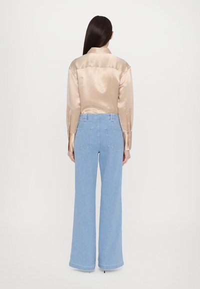 Light beige satin shirt with a pointed collar, buttoned cuffs, paired with high-waisted light blue flared jeans featuring back pockets.