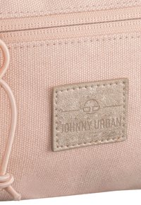 Persikofärgad tygpåse med en texturerad yta, som har ett metalliskt logopatch och en dragkedjestängning. Detaljer inkluderar eldgummi-kord.