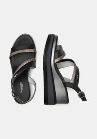 Black sandal with metallic accents, featuring wide cross-straps, a chunky wedge heel, and a secure ankle strap with buckle closure.