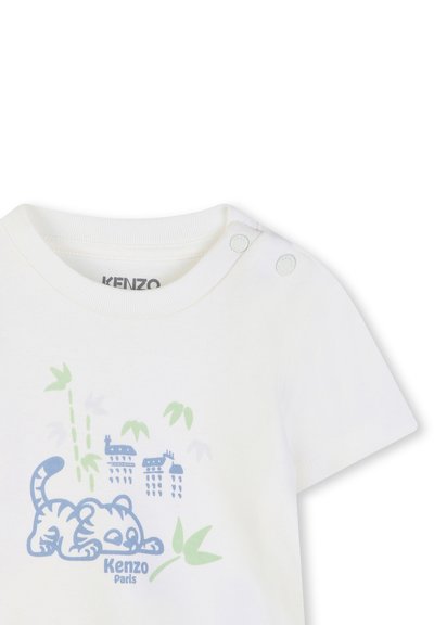 T-shirt blanc à manches courtes avec un motif de tigre bleu, du bambou vert, et des bâtiments bleu clair. Boutons-pression à l'épaule pour un habillage facile.