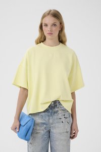 Ung kvinde iført en løs bleg gul t-shirt og falmede mønstrede jeans, som holder en lille klarblå, blød clutchtaske.