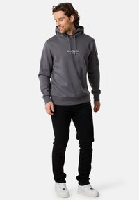 Felpa grigia con tasca a marsupio frontale, coulisse e logo bianco stampato. Abbinata a jeans neri e sneaker bianche.