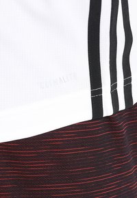 White athletic shirt with black stripes and a ribbed texture. Features "Climalite" branding, paired with red and black striped shorts.