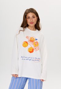 Witte lange mouw t-shirt met oranje vrucht graphics en blauwe tekst. Het shirt heeft een relaxte pasvorm en zachte stof. Casual ontwerp.
