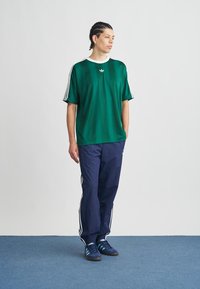 Zelena košulja kratkih rukava s bijelim ovratnikom, uparena s mornarsko plavim hlačama s bijelim bočnim prugama i plavim cipelama s crnim potplatima.