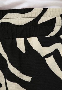 Juodas ir kremas raštuotas audinys su tekstūriniu, banginiu raštu. Elastinga juosmens juosta su matomomis siūlėmis. Minkšta, šiek tiek pūkuota tekstūra.