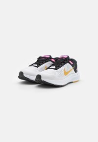 Scarpe da ginnastica bianche con una parte superiore in rete traspirante, accenti neri, dettagli rosa sui lacci e un logo a profilo dorato. Suola in gomma.