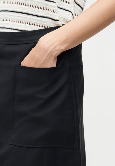 Χέρι που εισέρχεται στην μπροστινή τσέπη μιας μαύρης φούστας που φοριέται με λευκό και μαύρο ριγέ πλεκτό τοπ.