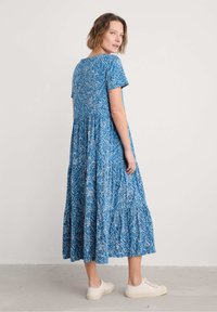 Robe maxi à motif floral bleu avec des manches courtes, design à volants et coupe décontractée, associée à des baskets de teinte neutre.