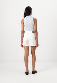 Lichtblauwe geribbelde mouwloze top gecombineerd met witte high-waisted shorts. De shorts hebben twee achterzakken en een zwart label op de taille.