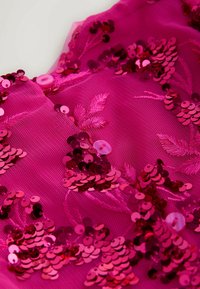 Pink tylstof dekoreret med rosenfarvede pailletter, pailletblomster og en gennemsigtig tekstur, med en rund knapdetalje.