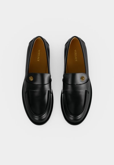 Ζευγάρι μαύρα δερμάτινα loafers Versace με χρυσά κουμπιά Medusa, εμφανιζόμενα από πάνω σε απλό λευκό φόντο.