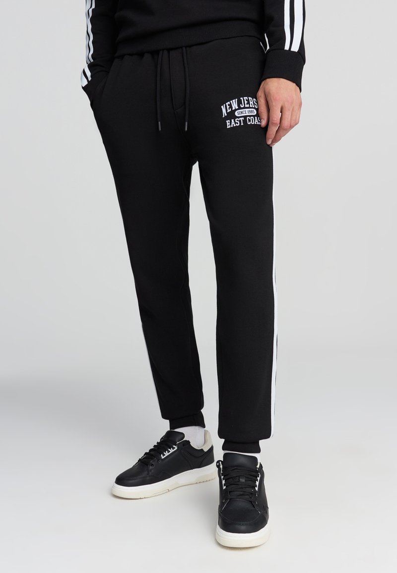 Czarne dresy z białymi bocznymi paskami, z haftowanym logo "New Jersey East Coast", elastycznym paskiem w talii i ściągaczami na kostkach.